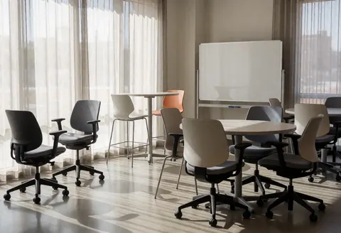 Bright modern university study hall featuring ergonomic chairs, round tables, and a whiteboard. Natural light fills the space through large windows, creating an ideal environment for focused study or collaborative team work.