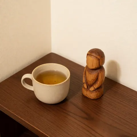 A ceramic tea cup and a small wooden figurine rest on a dark wooden table against warm walls, creating a calm and natural therapeutic atmosphere.