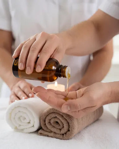 Close-up of hands with massage oil, towels, and a candle in a relaxing spa setting