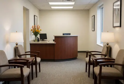 Modern online store reception featuring comfortable chairs, a wooden desk, computer, flowers, and natural light in a cozy interior.
