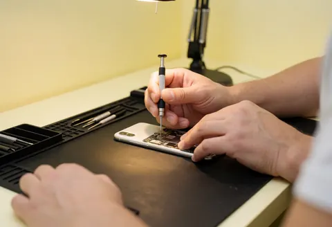 A technician's hands using a screwdriver to repair a mobile phone device in a professional electronics service setting
