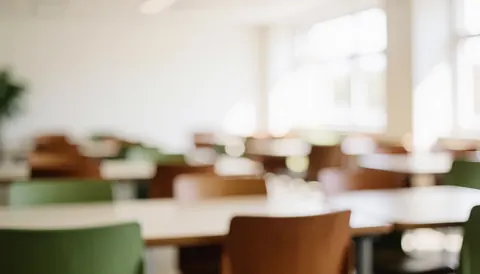Soft focus background of a university cafeteria interior featuring wooden tables and chairs under warm natural lighting, ideal for text overlays.