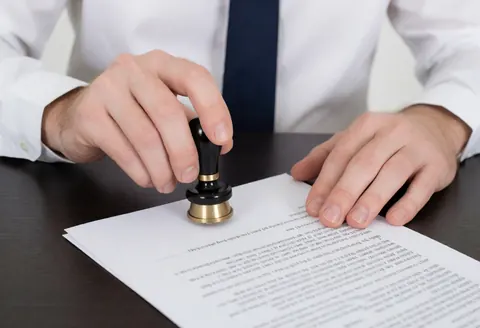 Lawyer's hand using a stamp on a legal document at a dark office desk, professional service in action