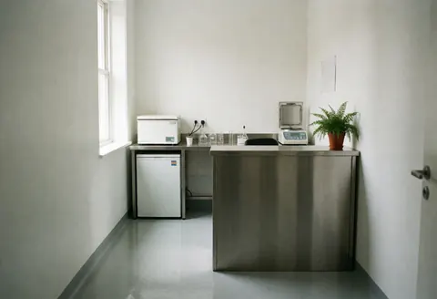 A clean and professional medical laboratory interior featuring stainless steel surfaces, a centrifuge, and a scale near a window with natural light