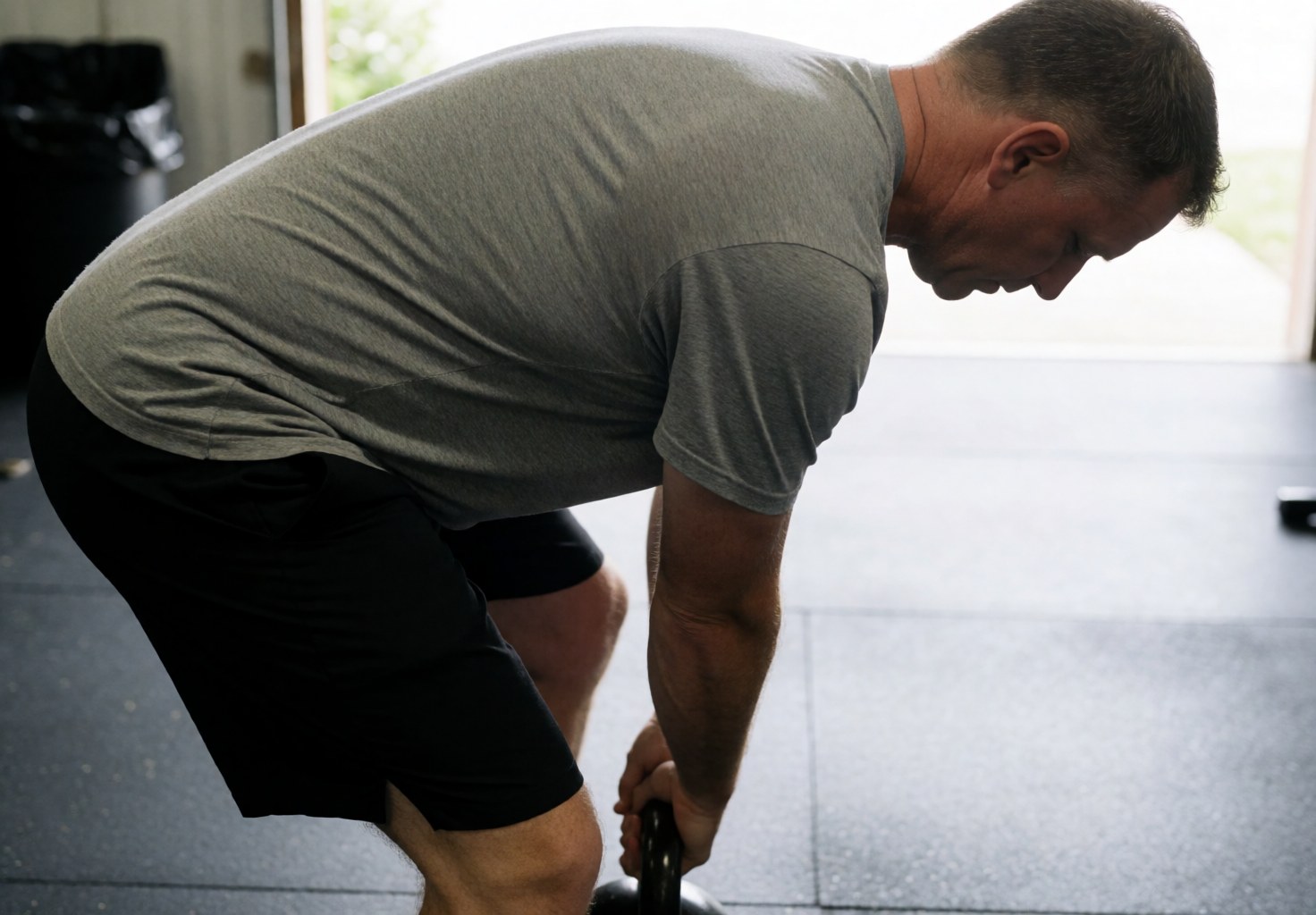 A man lifts a kettlebell with focus in a gym with rubber flooring and natural light, showing realistic and professional fitness action.