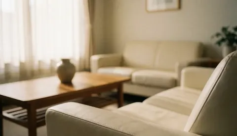A clean and calm therapy office interior featuring a beige sofa, wooden coffee table, and natural light from a window, ideal for text overlay.
