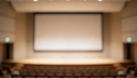 Soft focus view of a professional auditorium with a large screen and seating, serving as a clean backdrop for corporate text and business presentations.