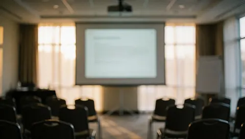 A softly blurred background of an empty conference room featuring chairs, a projector screen, and windows, ideal for text overlays in business presentations and training materials.