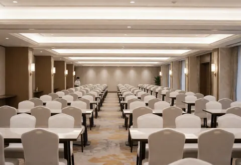 An elegant empty event hall featuring round tables with white tablecloths, chairs, and warm lighting against neutral walls.