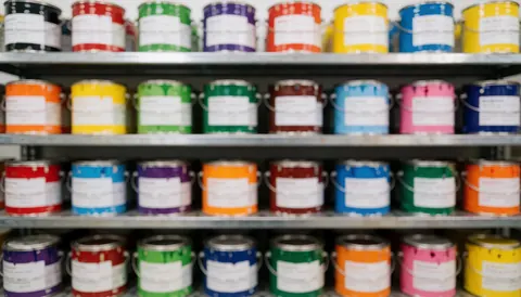 Rows of vibrant paint cans neatly arranged on industrial metal shelving units, providing a clean and organized background suitable for hardware store marketing and commercial text overlays.