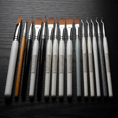 Set of professional nail art brushes and tools arranged neatly on a dark wooden table with dramatic lighting, ideal for beauty salons
