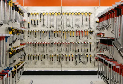 A well-organized hardware store aisle displaying various hand tools, wrenches, screwdrivers, and hammers hanging on the wall for retail customers.