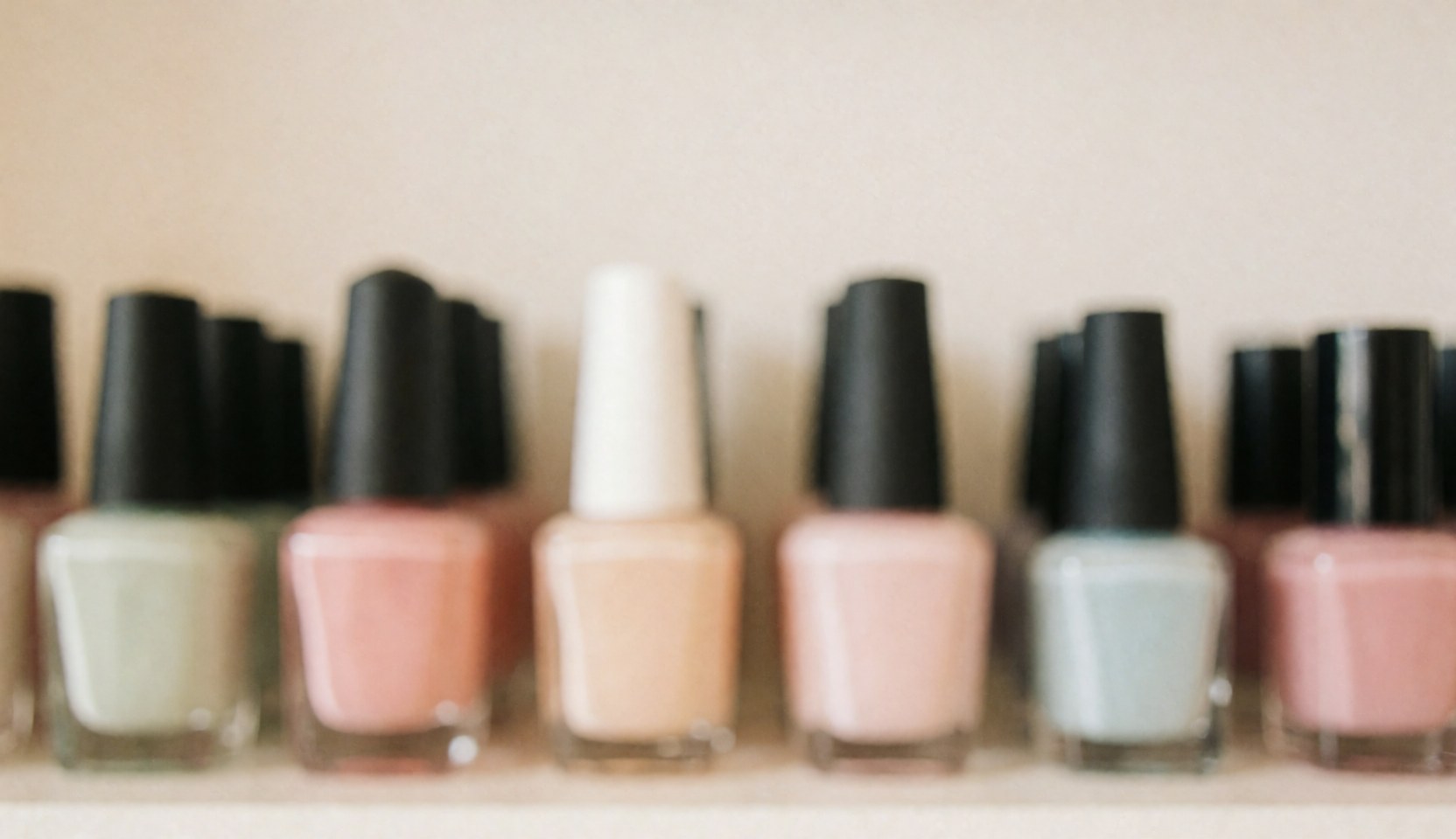 A soft, out-of-focus background featuring rows of colorful nail polish bottles, ideal for text overlay in nail salon marketing materials.