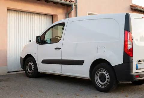 White pickup truck parked on asphalt in front of a residential garage with pale terracotta walls under soft afternoon light.