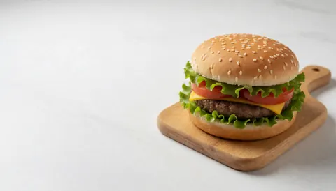 A fresh hamburger with lettuce, tomato, and cheese on a wooden board against a white background, ideal for fast food menus and banners.