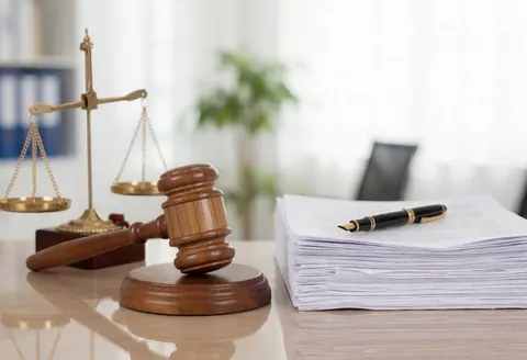 Bronze scales of justice and a wooden gavel resting on a tidy desk with legal documents and a pen, symbolizing law and order for a business.