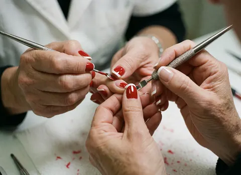 Close-up of a French manicure featuring metal tools, a brush, and scissors next to bright red nails on a clean professional background.