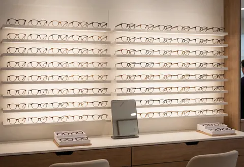 Wall of eyeglasses in an optical shop with soft lighting, clean counter, mirror, and glasses boxes