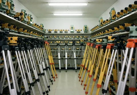 Organized storage room containing surveying tripods and equipment under fluorescent lighting, showcasing a professional and functional workspace for field work.