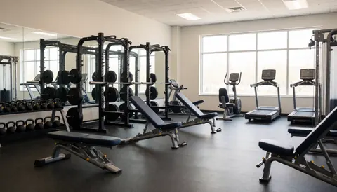 A wide, well-lit gym interior featuring various weight machines, dumbbells, and cardio equipment arranged neatly in a modern fitness facility.