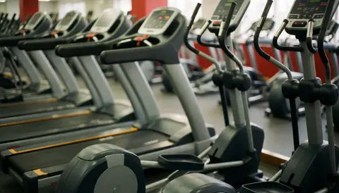 Out of focus gym interior featuring treadmills and elliptical trainers in gray and red tones, serving as a clean background for fitness text overlays