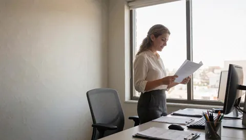 Professional accountant reviewing documents at a desk in a bright modern office near a window with computer and supplies