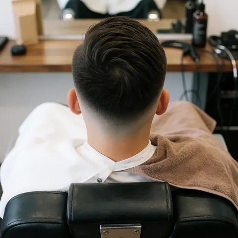 Close-up of a fresh modern fade haircut result displayed on a barber chair with a towel and grooming products nearby