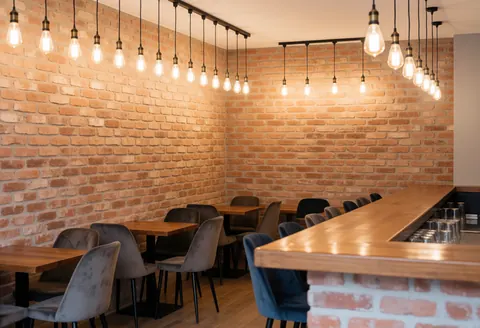 Interior view of a stylish bar featuring exposed brick walls, wooden furniture, and warm pendant lighting creating an inviting atmosphere