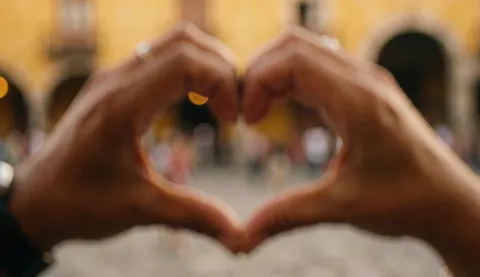 Hands forming a heart shape in a plaza with warm, blurred architecture, ideal for nonprofits and communities seeking to convey love and solidarity.