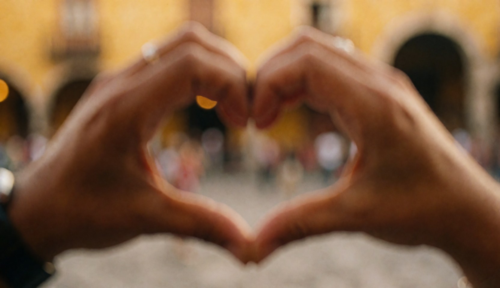 Hands forming a heart shape in a plaza with warm, blurred architecture, ideal for nonprofits and communities seeking to convey love and solidarity.