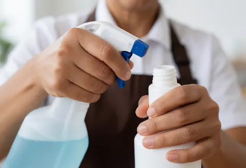 Close-up of hands mixing cleaning solution in a spray bottle, blurred background, clean lighting for commercial or residential cleaning services