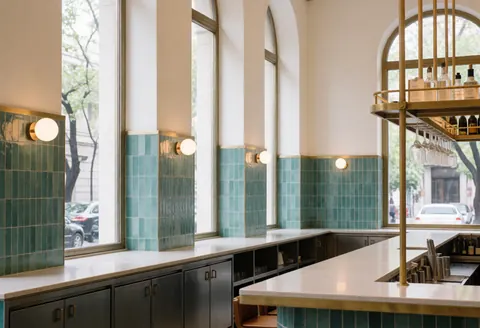 Modern bar interior featuring turquoise tiles, bronze details, large windows, clean bar counter, warm lighting, and elegant atmosphere without people.
