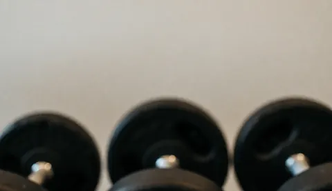 A dark, out-of-focus background featuring blurred gym dumbbells, providing a professional and abstract space suitable for overlaying text or business content.