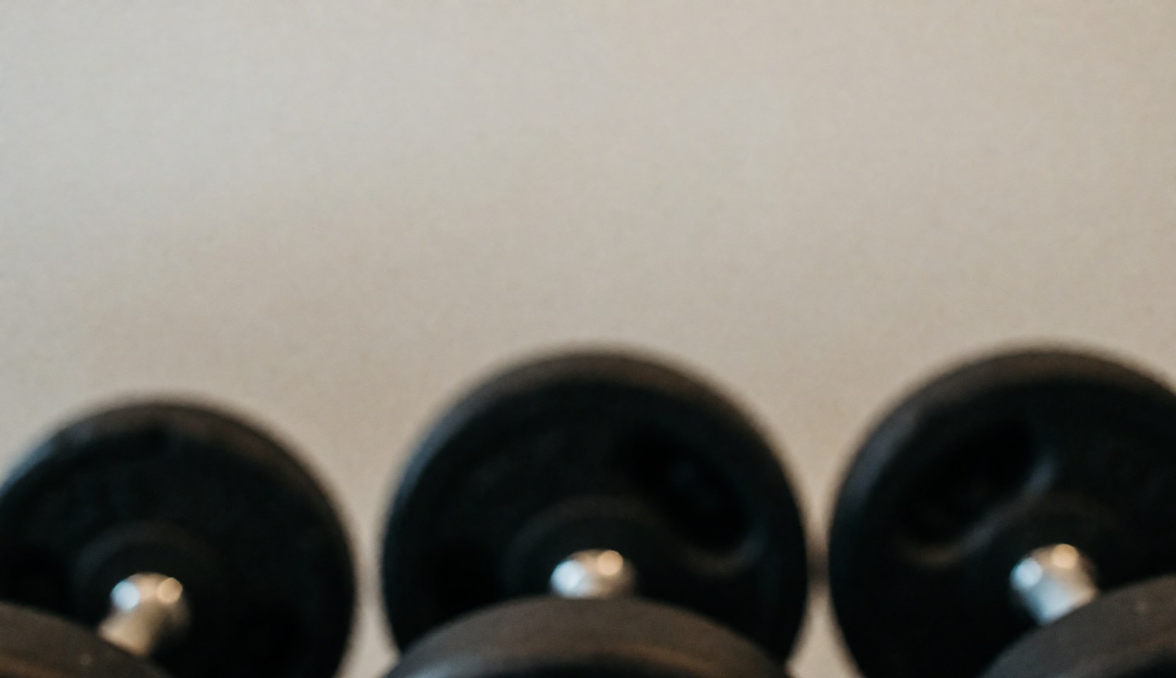 A dark, out-of-focus background featuring blurred gym dumbbells, providing a professional and abstract space suitable for overlaying text or business content.