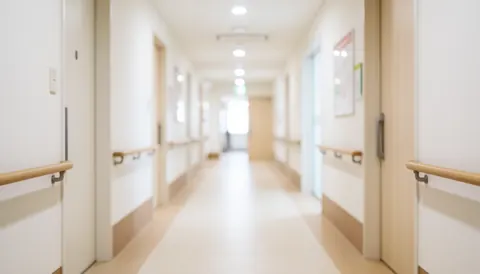 A blurred view of a clean and calm medical clinic hallway with beige walls, white doors, and soft lighting, serving as a professional background for healthcare content