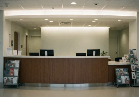 Clean medical clinic reception with wooden desk, monitors, brochures, and soft lighting. Professional and tidy interior space.