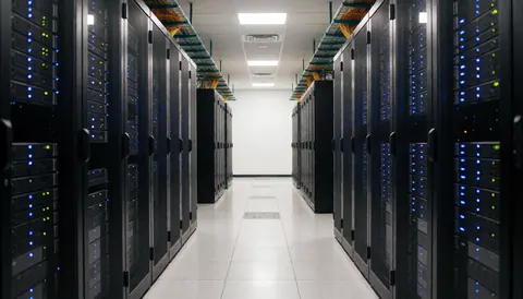 A clean server aisle in a data center featuring blue indicator lights, exposed ceiling cabling, and a polished floor.