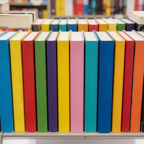 Colorful paperback books with bright covers arranged on a bookstore shelf under clean, bright lighting, ideal for promoting a bookstore or book shop.