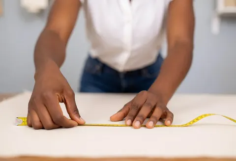 Close-up of hands using a measuring tape on fabric rolls in a workshop setting for garment manufacturing