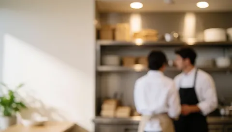 Restaurant kitchen background featuring staff, stainless steel shelves, and warm lighting with copy space on the left