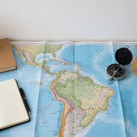 Flat lay of a South America map, compass, notebook, and pen on a white surface for travel planning