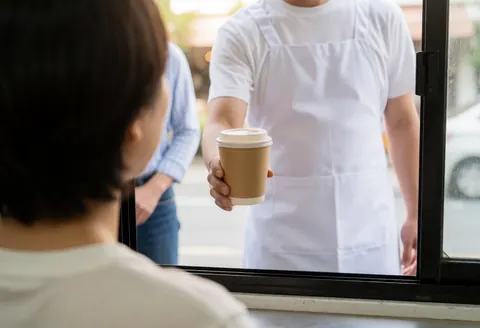 A vendor in a food truck serves a cup of coffee to a customer from behind, with soft morning light creating a realistic and professional atmosphere.