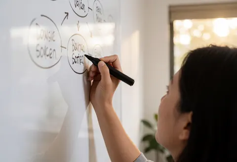 Professional woman writing a mind map on a whiteboard in a modern office with natural light, ideal for online courses and virtual education.