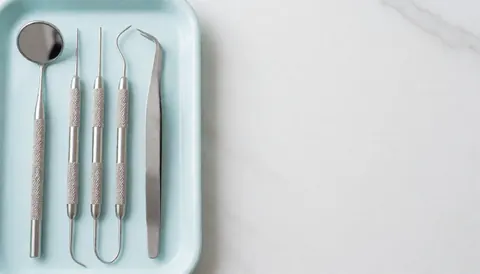 Sterile dental tools arranged on a blue tray against a white background, suitable for dental clinic advertising and text overlays