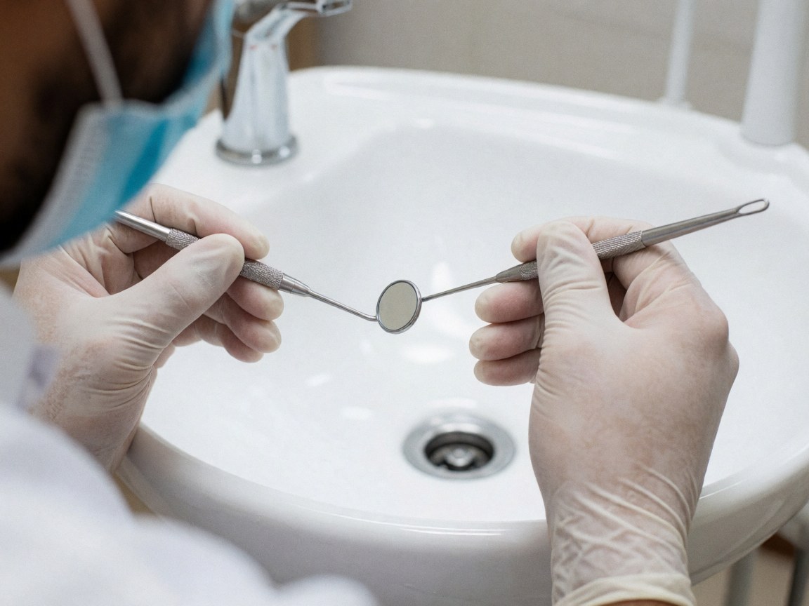 Dentist hands in gloves adjusting a dental mirror and explorer over a white sink in a clean clinical setting