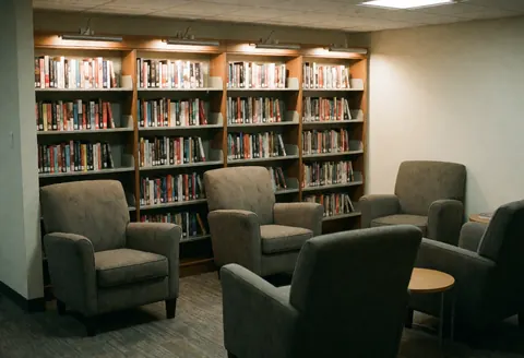 Cozy reading nook featuring comfortable armchairs and bookshelves filled with books, offering a warm and quiet atmosphere for coworking.