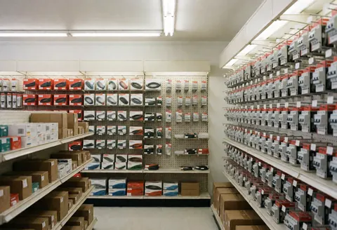 Clean interior of an empty electrical store with shelves stocked with wires, switches, and product boxes under fluorescent lighting.