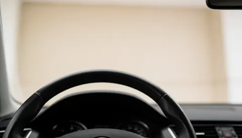 Soft focus view of a European car dashboard and steering wheel, providing a clean neutral background suitable for text overlay in driving school materials.