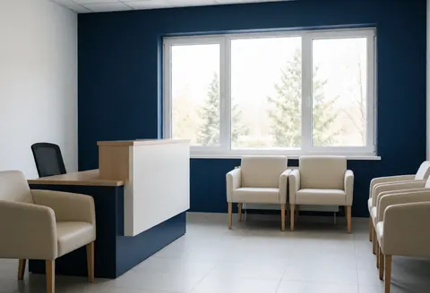Clean modern driving school reception featuring a counter, waiting chairs, large windows with natural light, blue walls, and white tile floor