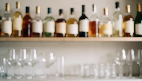 Out-of-focus bar shelf displaying liquor bottles and wine glasses with warm neutral tones, suitable for cocktail marketing text backgrounds